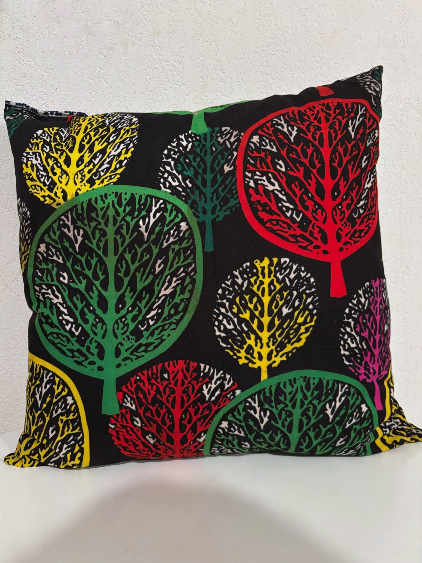 Coussin en wax avec motifs colorés d'arbres sur fond noir, ajoutant une touche moderne à la décoration intérieure.