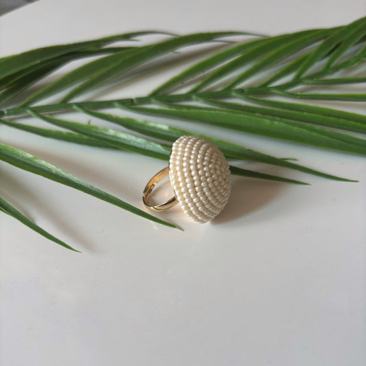 Bague perles élégante sur fond blanc, entourée de feuilles, un bijou parfait pour chaque occasion.
