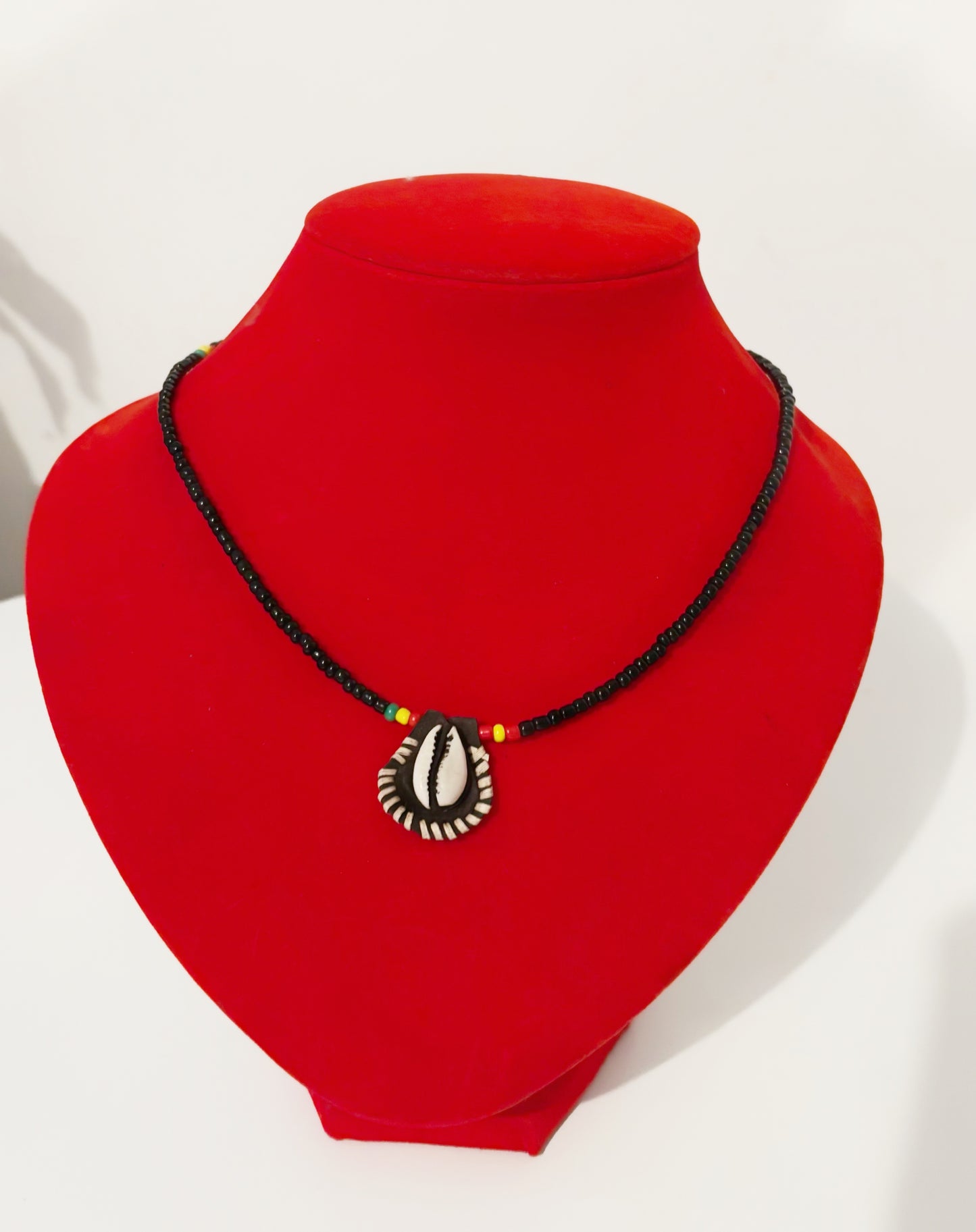 Collier en perles noires et pendentif cauri sculpté, bijou traditionnel africain sur support rouge.
