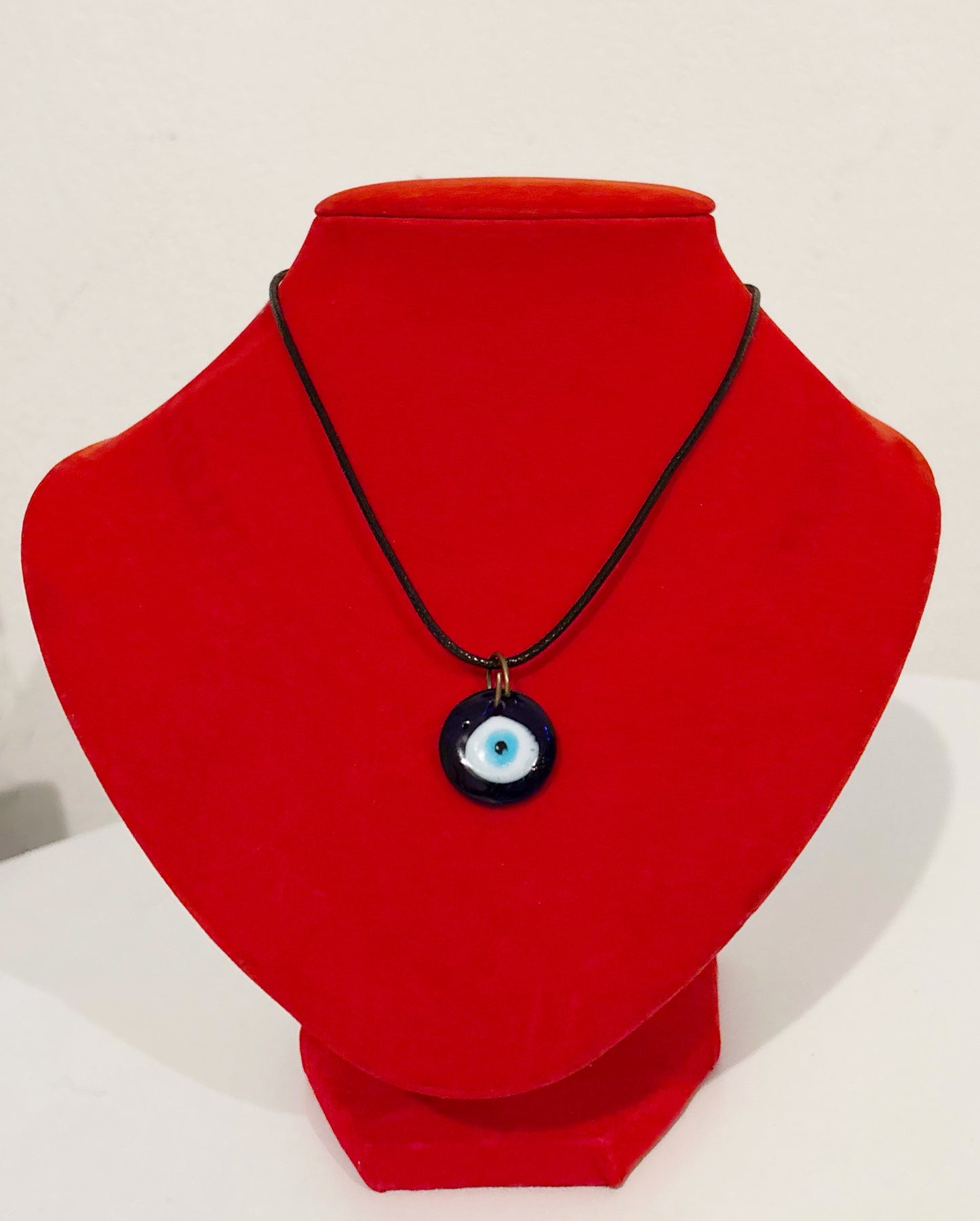 Collier porte bonheur en pierre avec pendentif œil bleu sur cordon noir, exposé sur un support rouge.